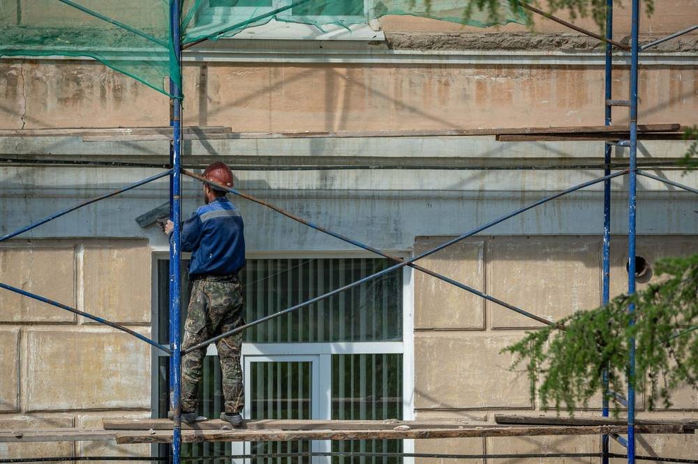 Altbausanierung: Handwerker arbeitet auf Gerüst an einer Gebäudefassade